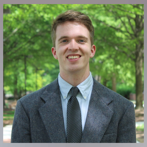 Blake Munshell's Headshot. He is a white male with blonde/brown/red hair, wearing a suit on a path outside the University of Maryland.